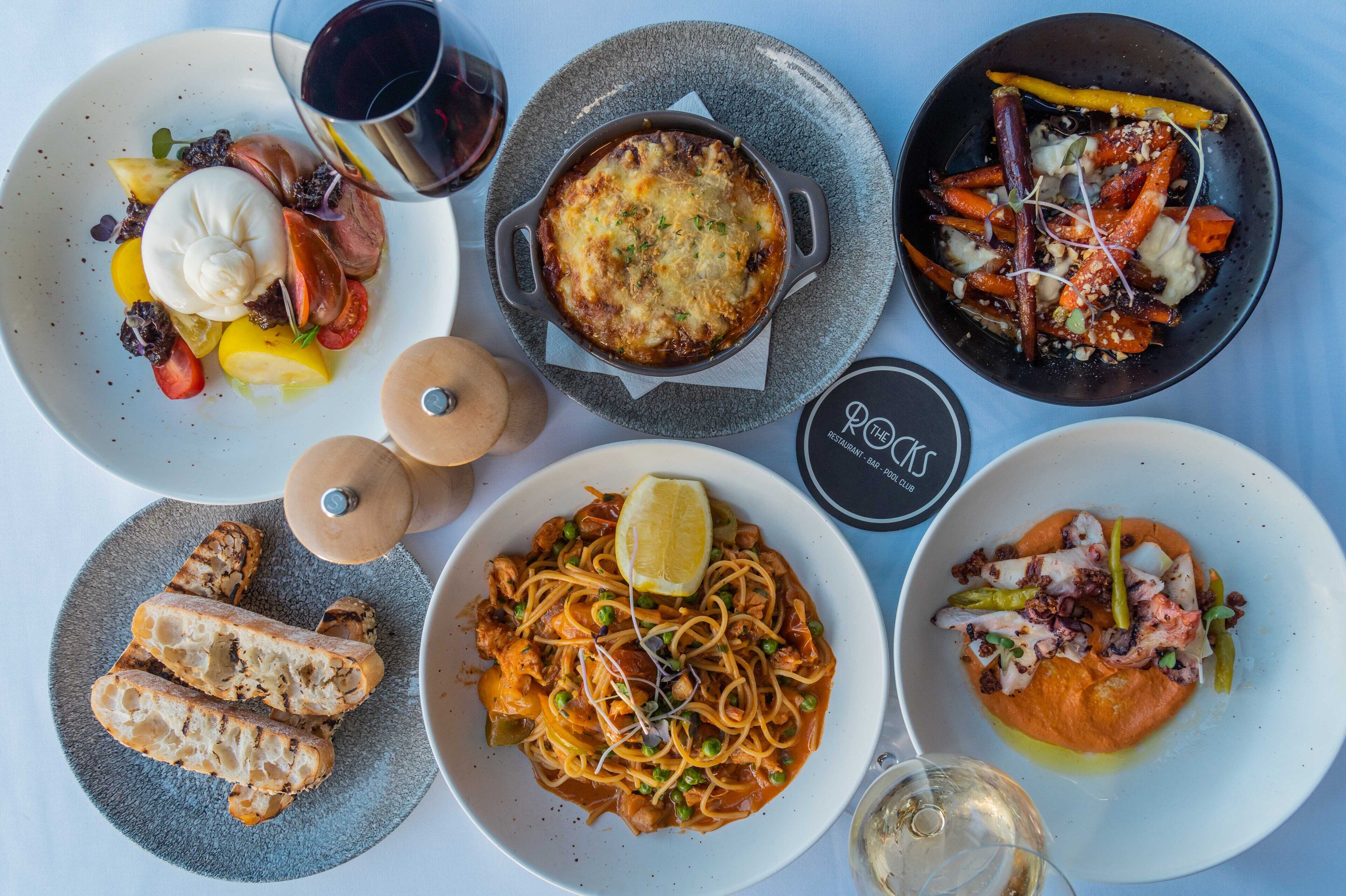 Variedad de platos que incluyen pasta, mariscos y verduras, servidos en distintas fuentes.