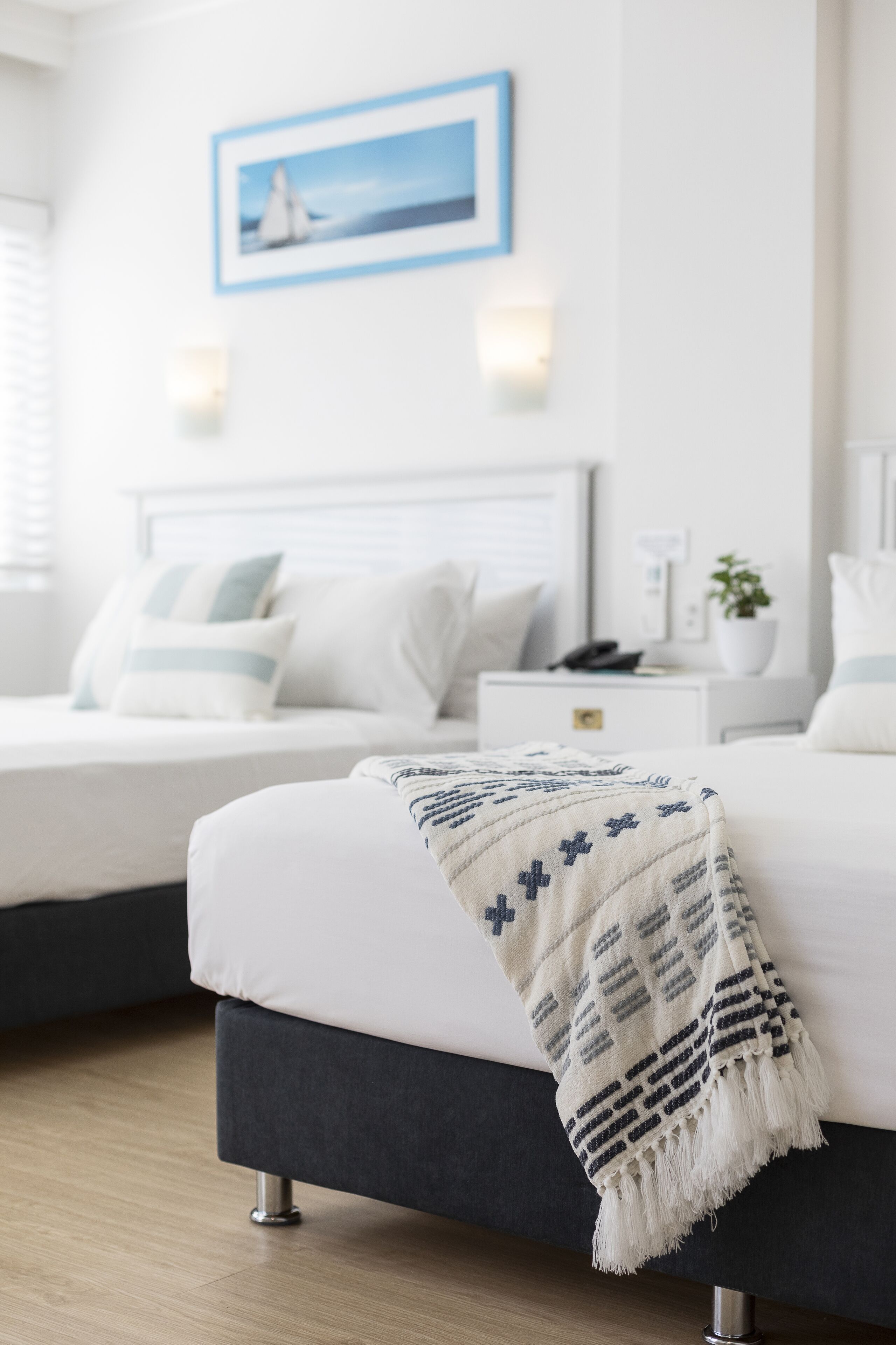 A modern bedroom with a large bed, a smaller bed, a nightstand, a wall-mounted lamp, and a framed picture.