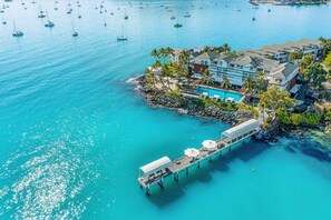 Vue aérienne d’un hôtel situé sur la côte, avec une piscine, une jetée et plusieurs bateaux sur l’eau.