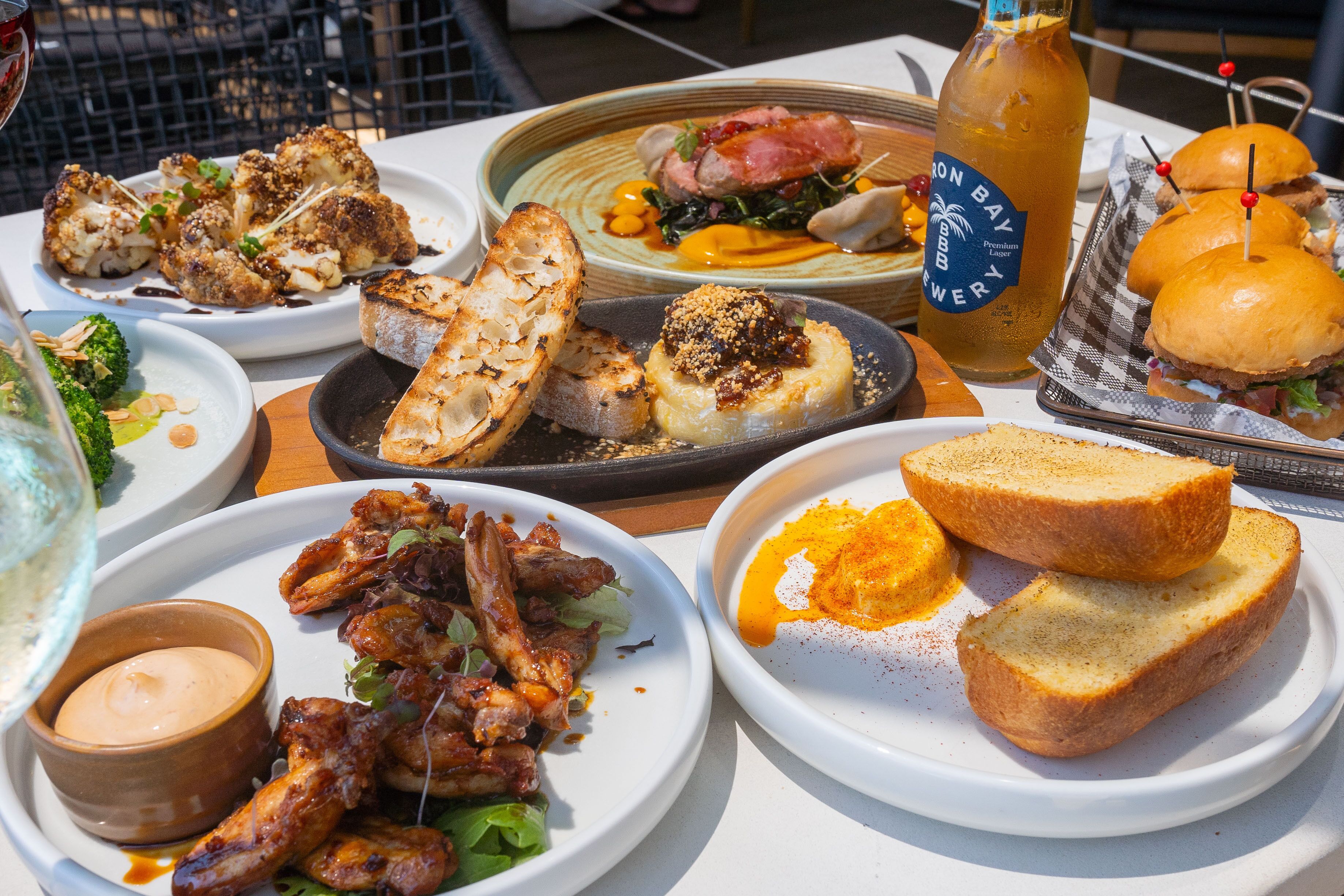 A table with various dishes including grilled chicken, bread, and a bottle of Iron Bay beer.