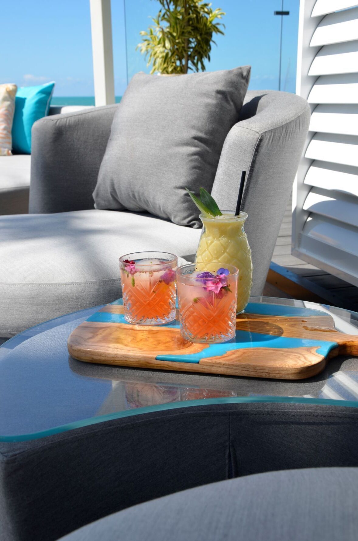 Ein Glas tropisches Getränk mit Strohhalm auf einem Holzboden, ein Glas Eistee mit einer Blume und ein Glas Orangensaft auf einem Tisch.