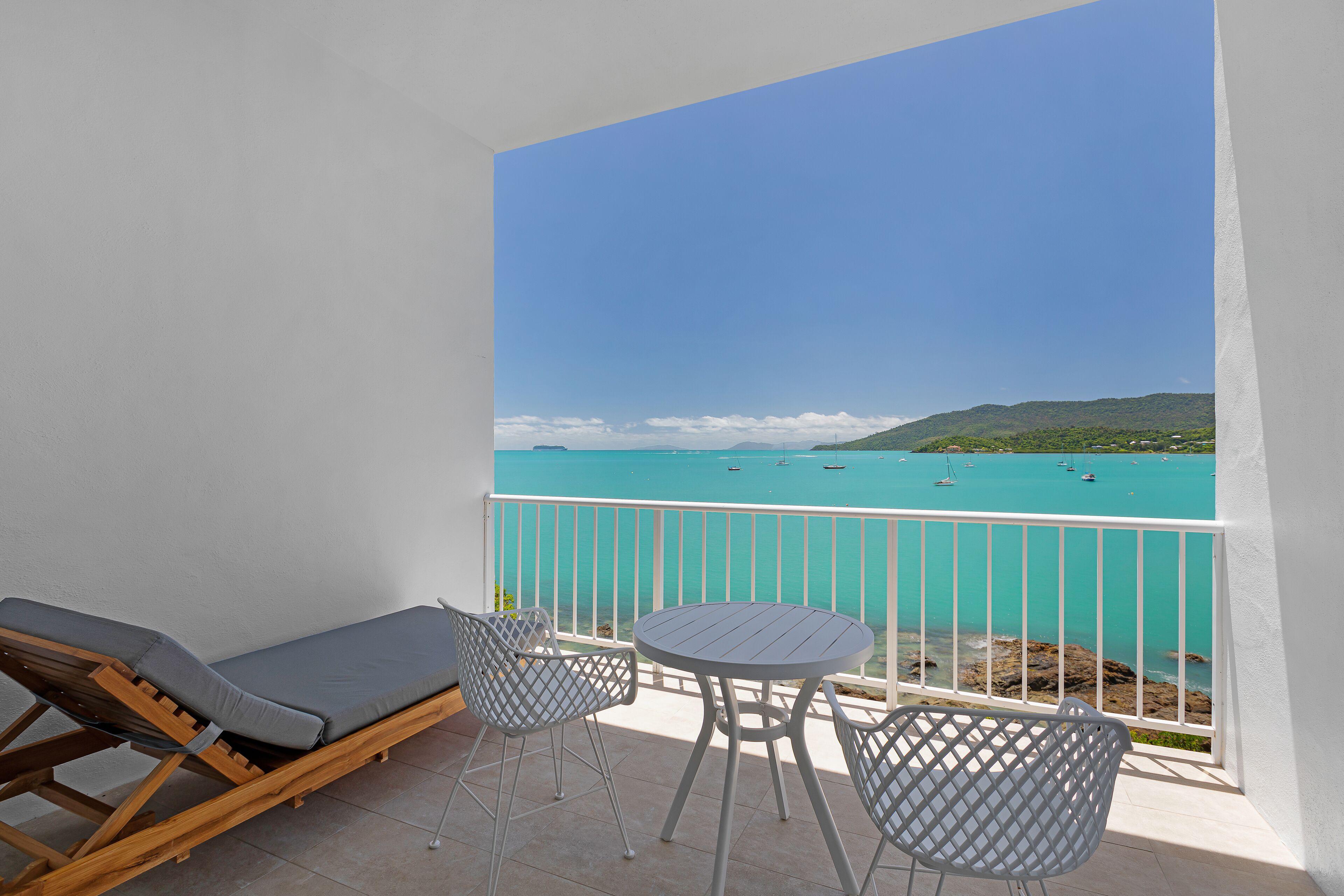 A balcony with a view of the sea, a lounge chair, and a small table.