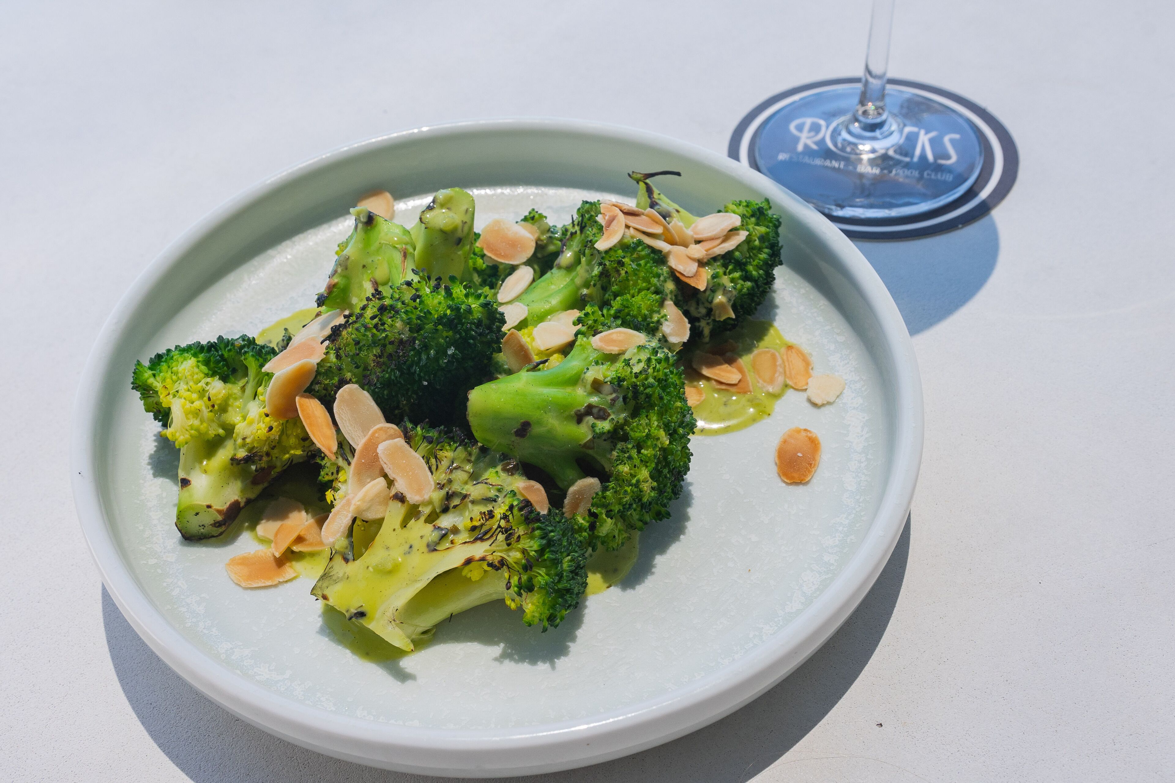 Un plato de brócoli con almendras sobre una mesa blanca.