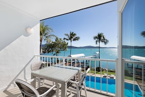 A balcony with a glass door, a pool, and a view of the ocean and palm trees. - Coral Sea Resort (Airlie Beach)
