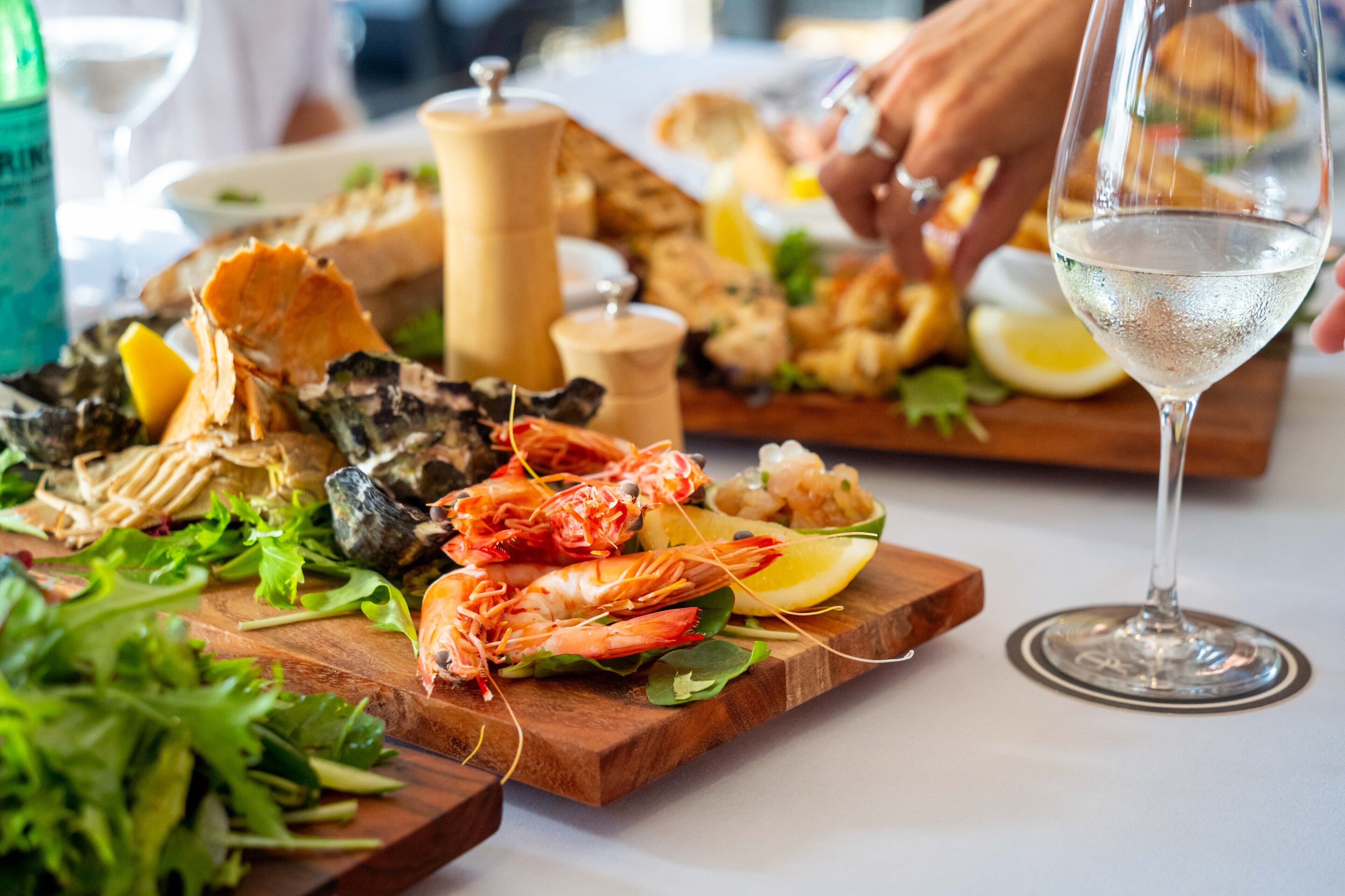 A seafood platter with shrimp, oysters, and lemon slices on a wooden board, accompanied by a glass of white wine.