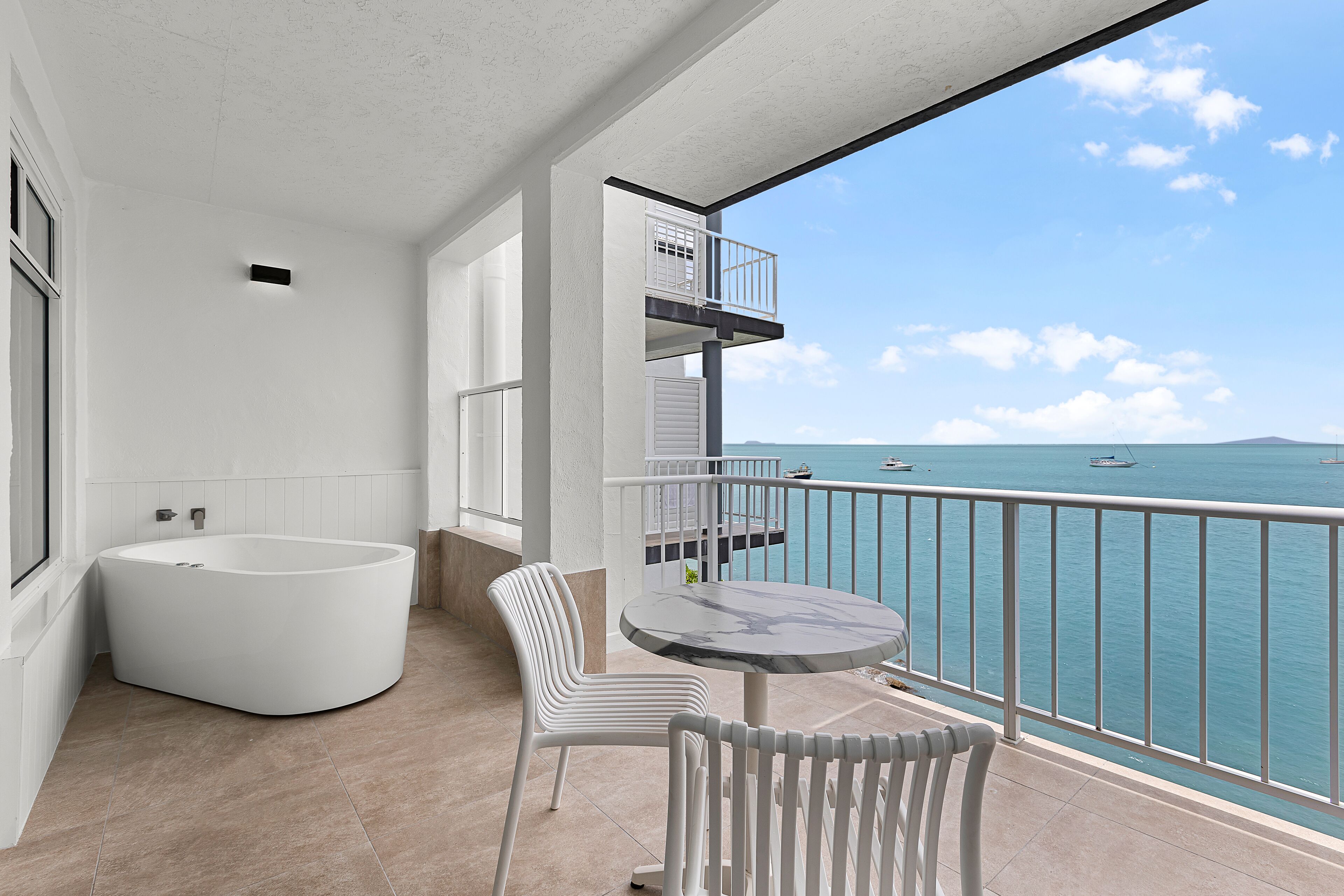 A balcony with a view of the sea, a bathtub, and a table with chairs.