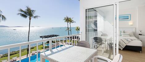 A balcony with a glass door leading to a bedroom, a pool, and a view of the sea.