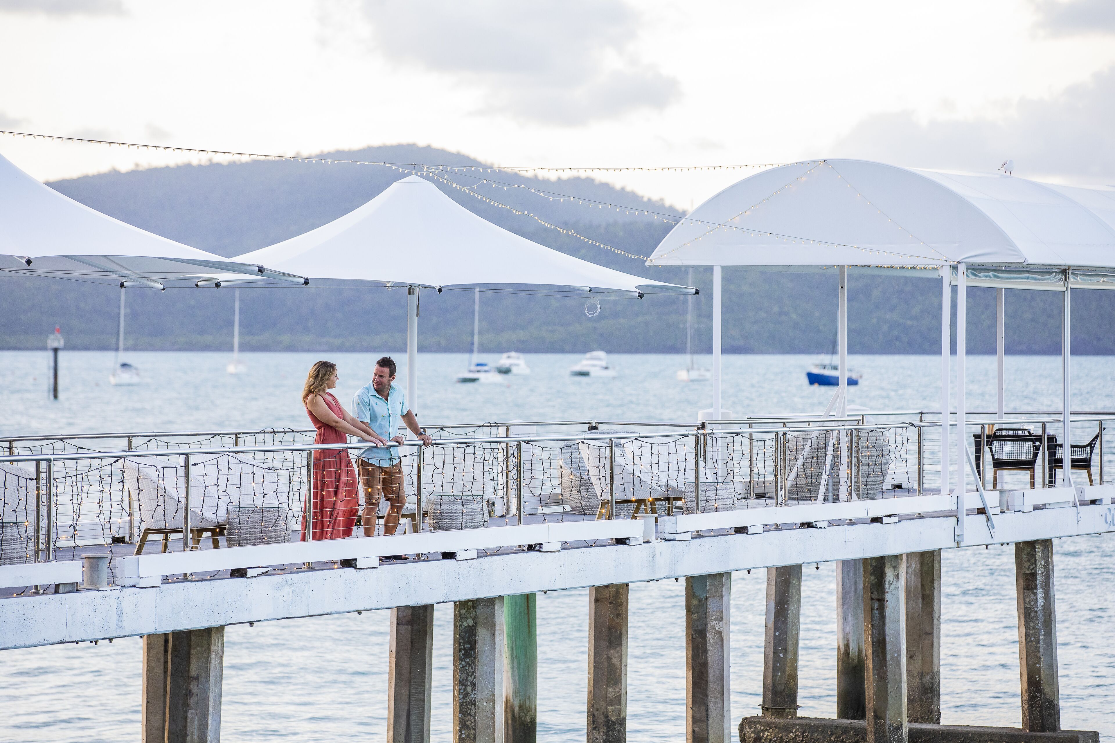 A pier with white canopies and chairs overlooking a lake with boats.