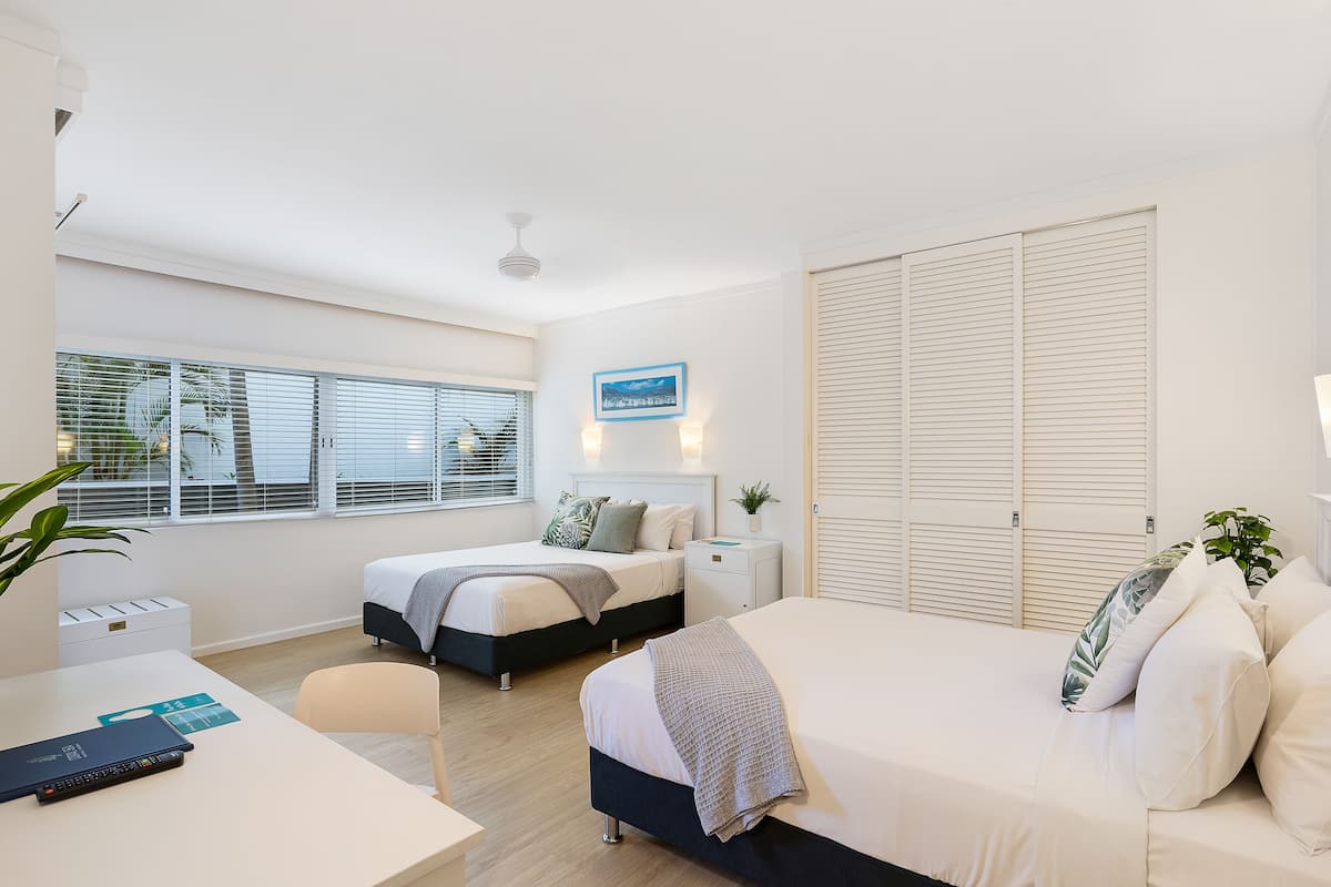Een moderne hotelkamer met twee bedden, een bureau en een groot raam met zonwering.