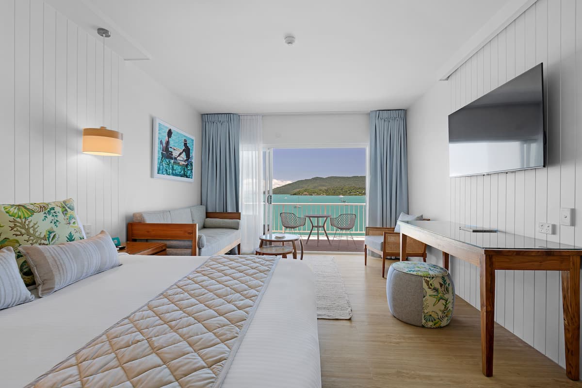 Hotelkamer met een bed, een bureau, een televisie, een balkon met uitzicht op zee en een eethoek.