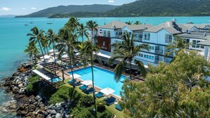 Un resort con piscina, palmeras y vista al mar.