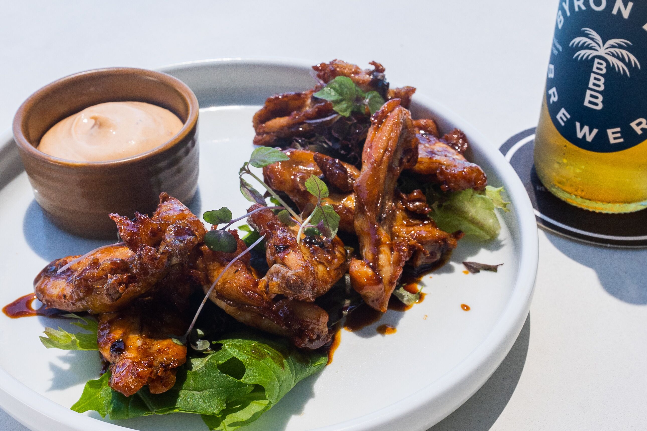 A plate of chicken wings with a side of sauce and a beer bottle.