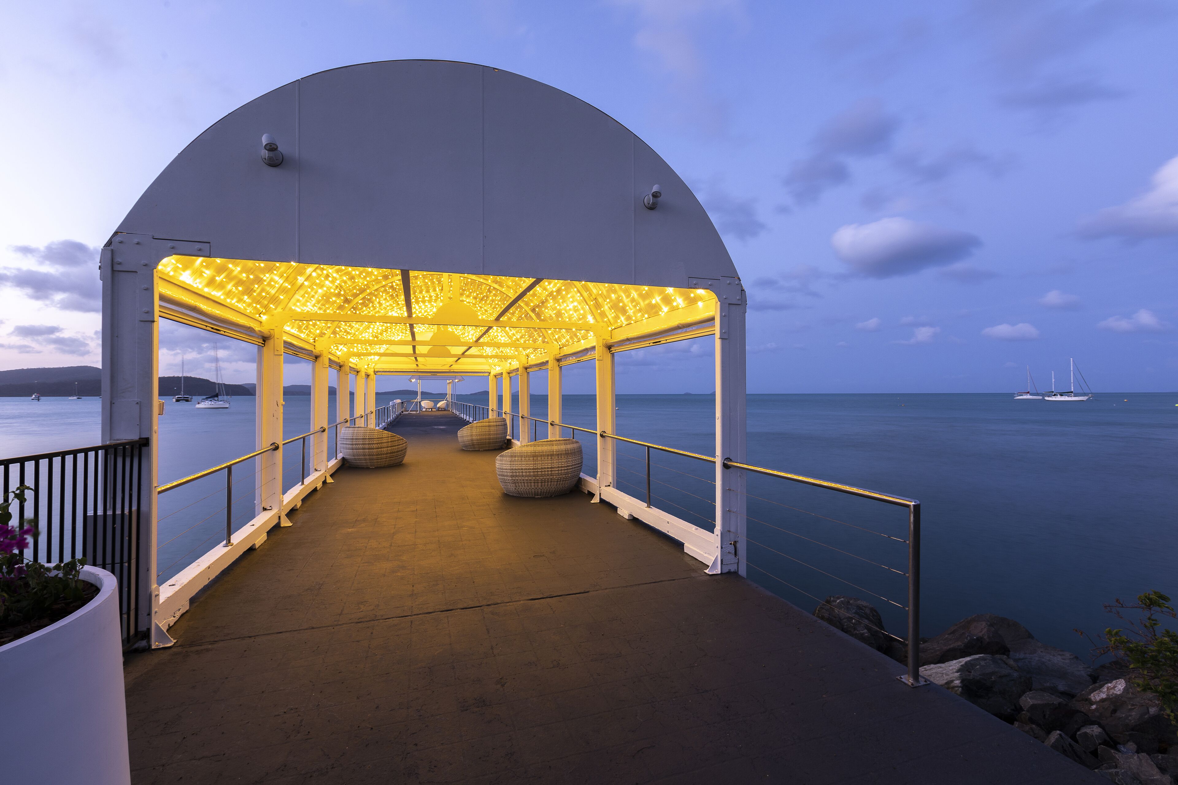 Une allée couverte offrant une vue sur la mer, agrémentée d’une rambarde et de coins salon.