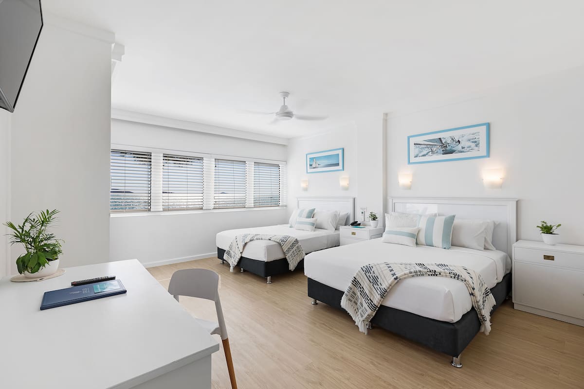 Een moderne slaapkamer met twee bedden, een bureau en een stoel. Er zijn twee nachtkastjes met lampen en een plafondventilator.