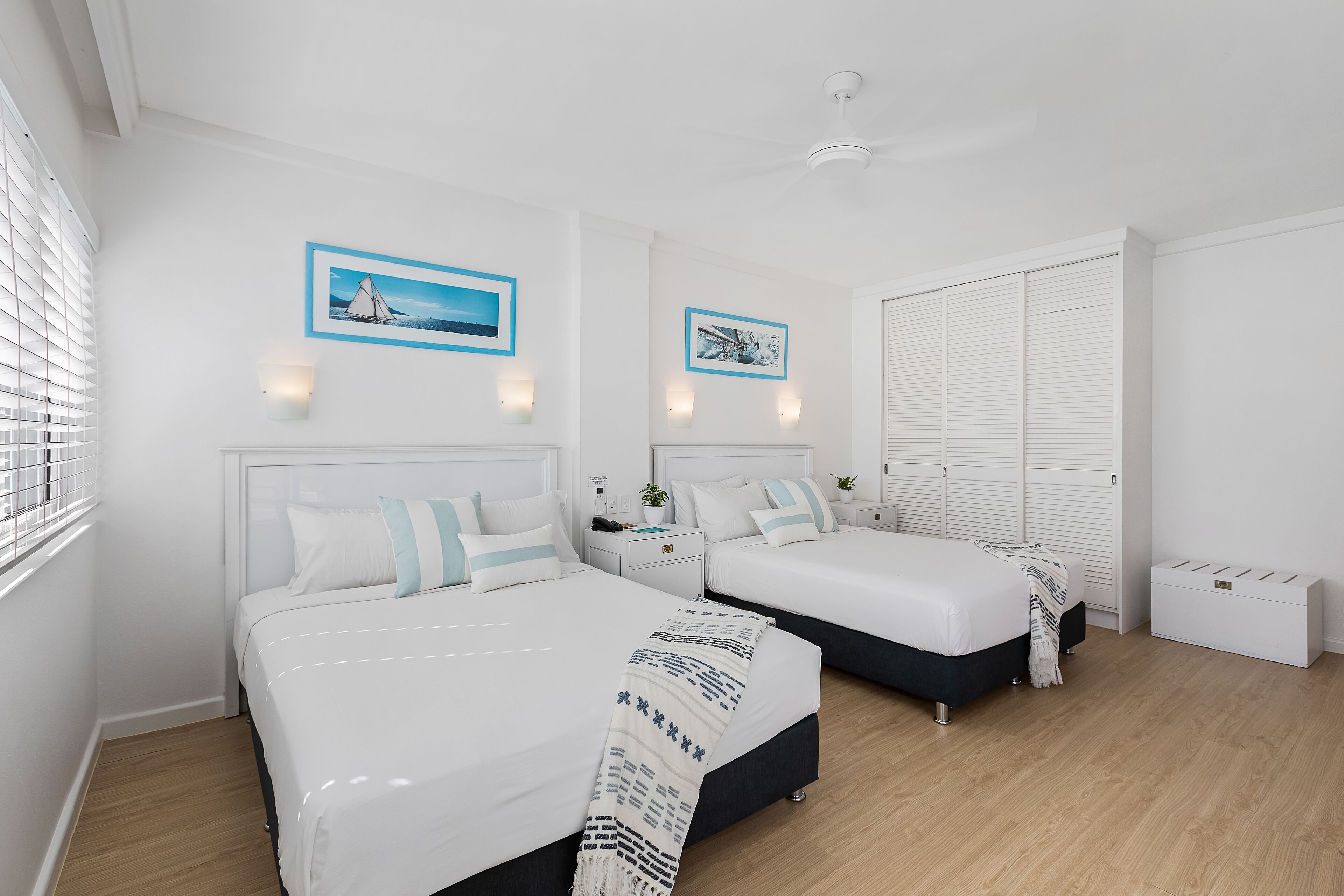 A modern bedroom with two beds, white bedding, and a wooden floor.