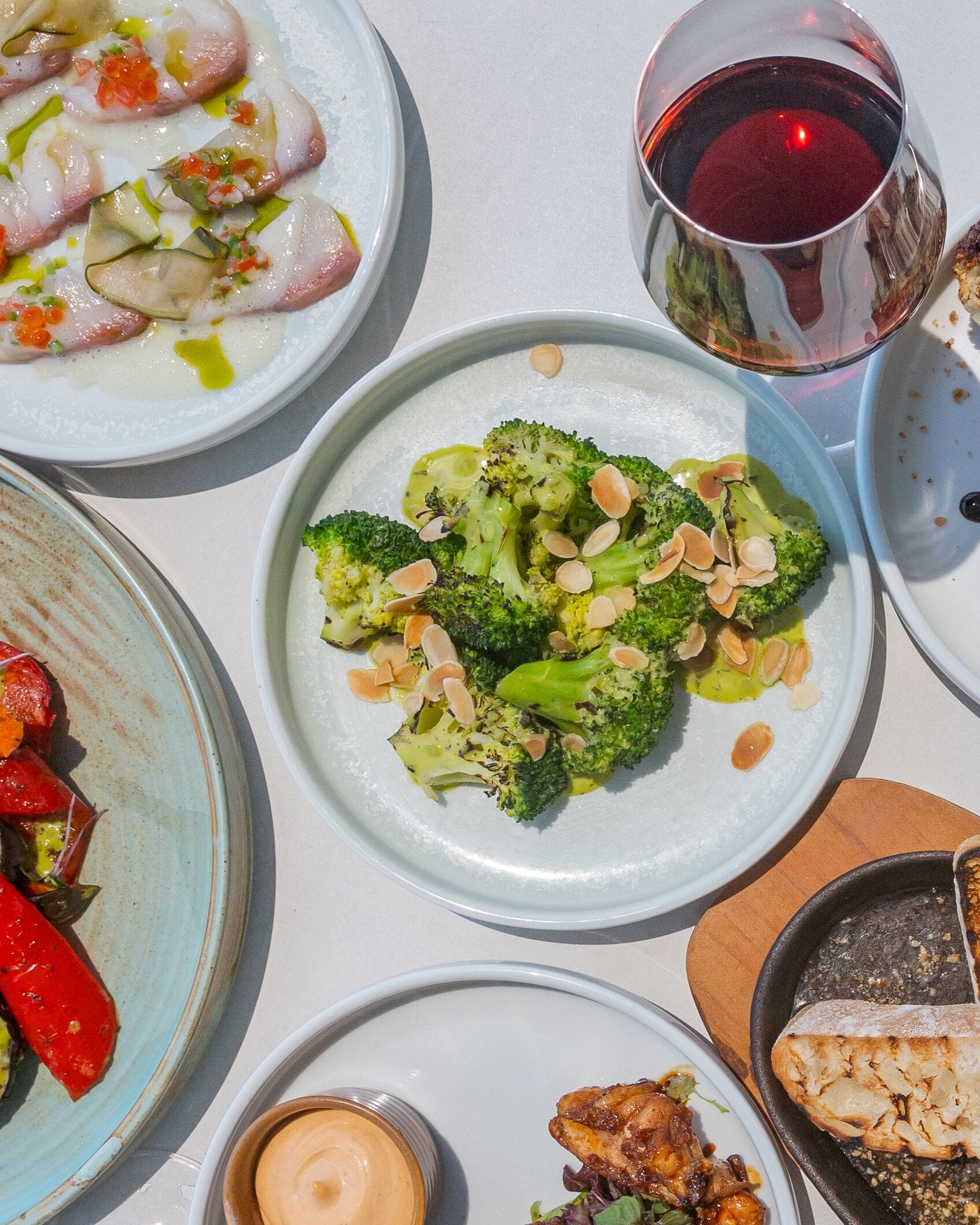 A table with various dishes including broccoli, a glass of red wine, and other food items.