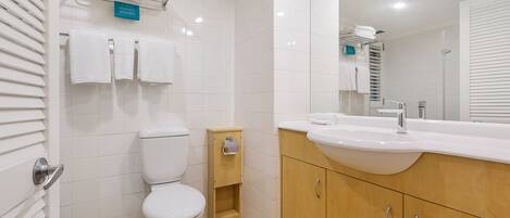 A modern bathroom with a toilet, sink, and mirror. There are towels on a rack and a small wooden cabinet.
