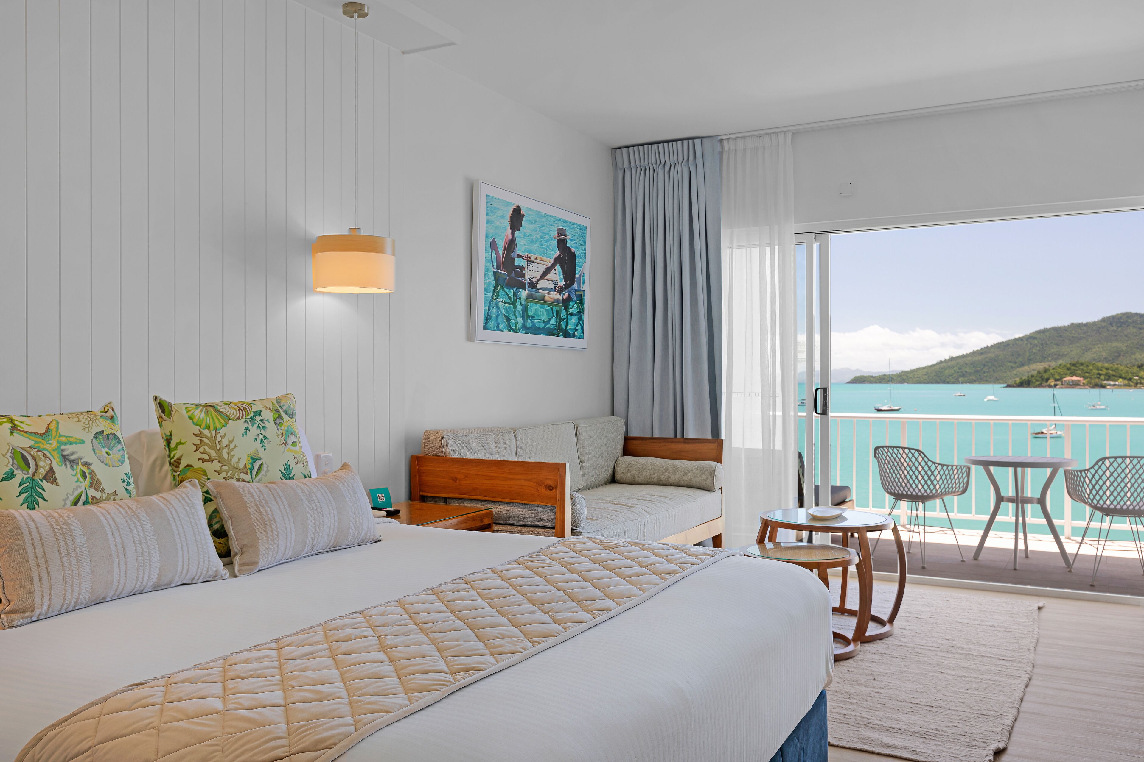 Habitación de hotel con una cama grande, un sofá, un balcón con vistas al mar y un cuadro en la pared.