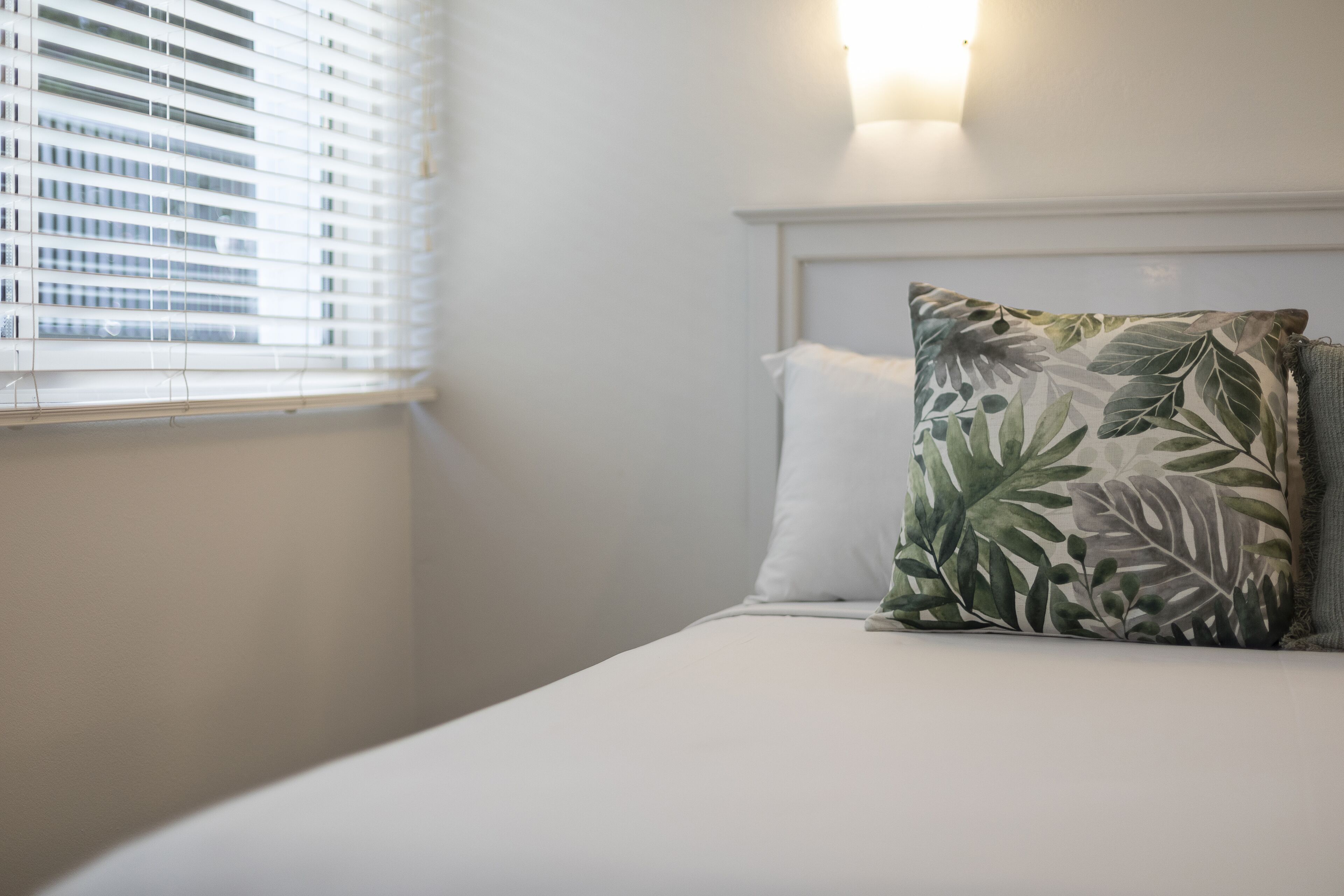Una habitación de hotel con una cama, una ventana con persianas y un aplique.