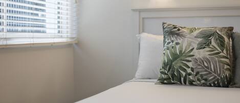 Una habitación de hotel con una cama, una ventana con persianas y un aplique.