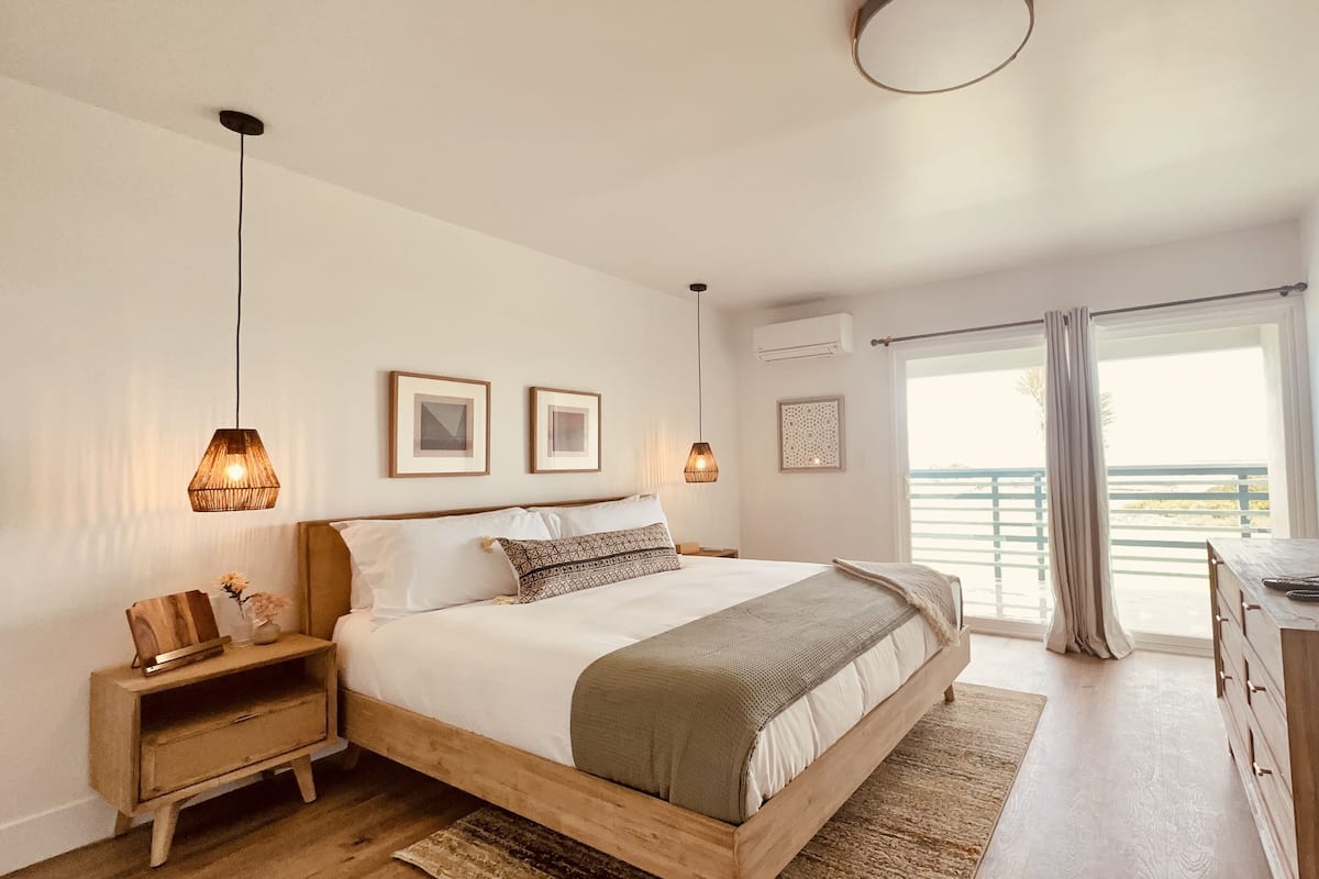 A bedroom with a bed, bedside tables, a desk, and a large window with a view.