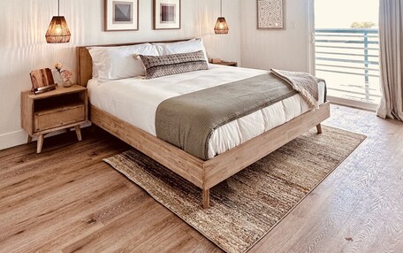 A bedroom with a wooden bed, two bedside tables, a large window with curtains, and two hanging lamps.