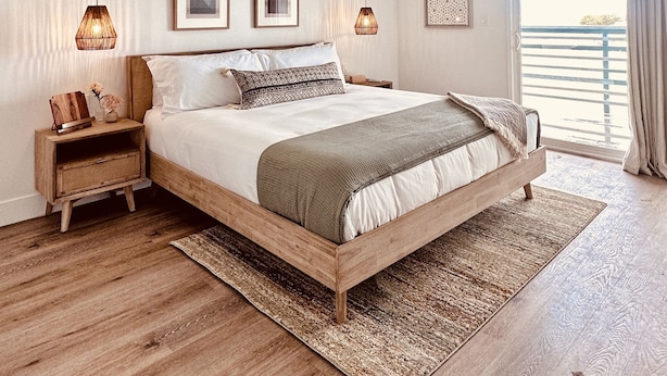 A bedroom with a wooden bed, two bedside tables, a large window with curtains, and two hanging lamps.