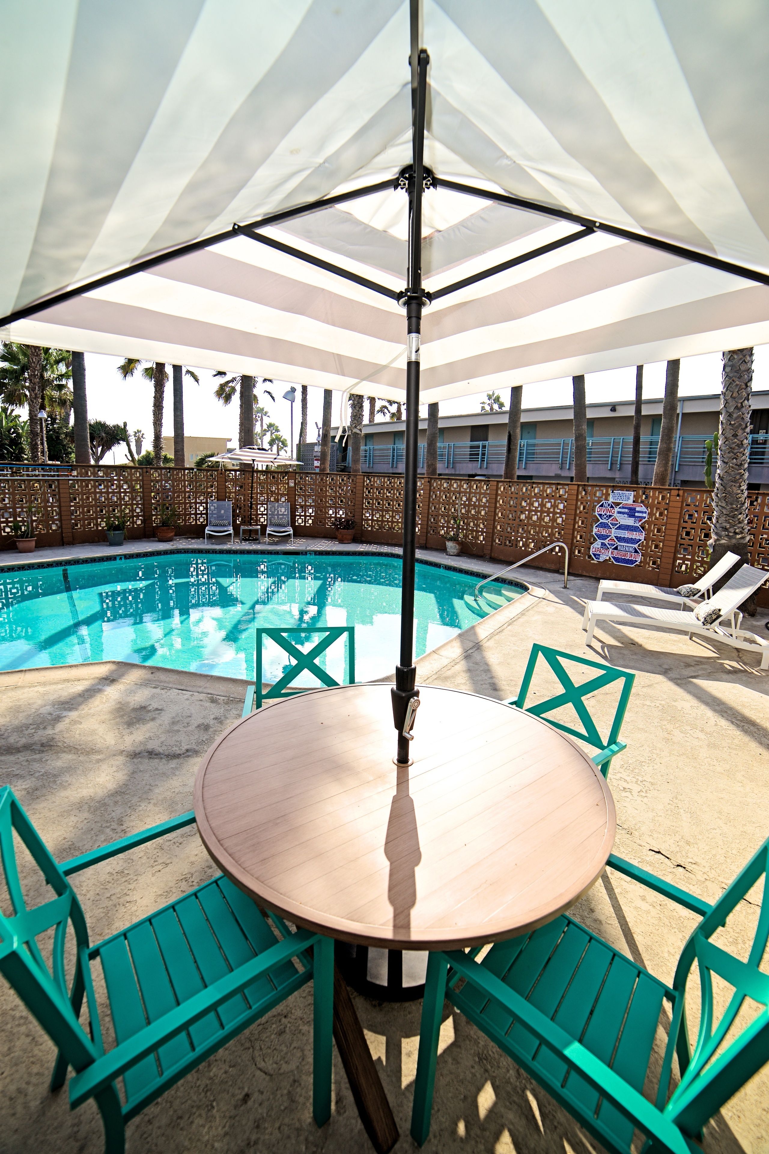 A poolside area with a round table and chairs, a large umbrella, and lounge chairs.