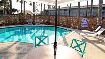 A poolside area with a round table and chairs, a large umbrella, and lounge chairs.