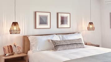Quarto com cama de madeira, duas mesas de cabeceira, um criado-mudo, tapete tecido e duas luzes pendentes.