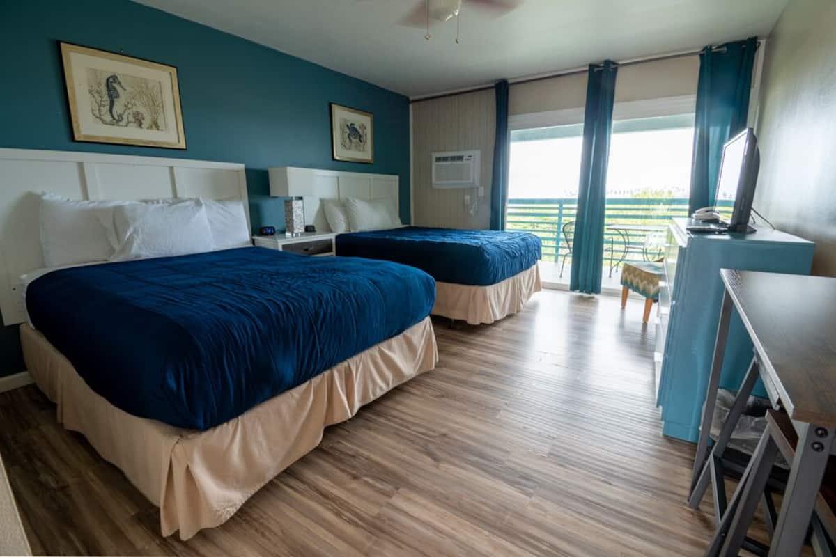 A hotel room with two beds, a desk, a chair, and a balcony with a view.