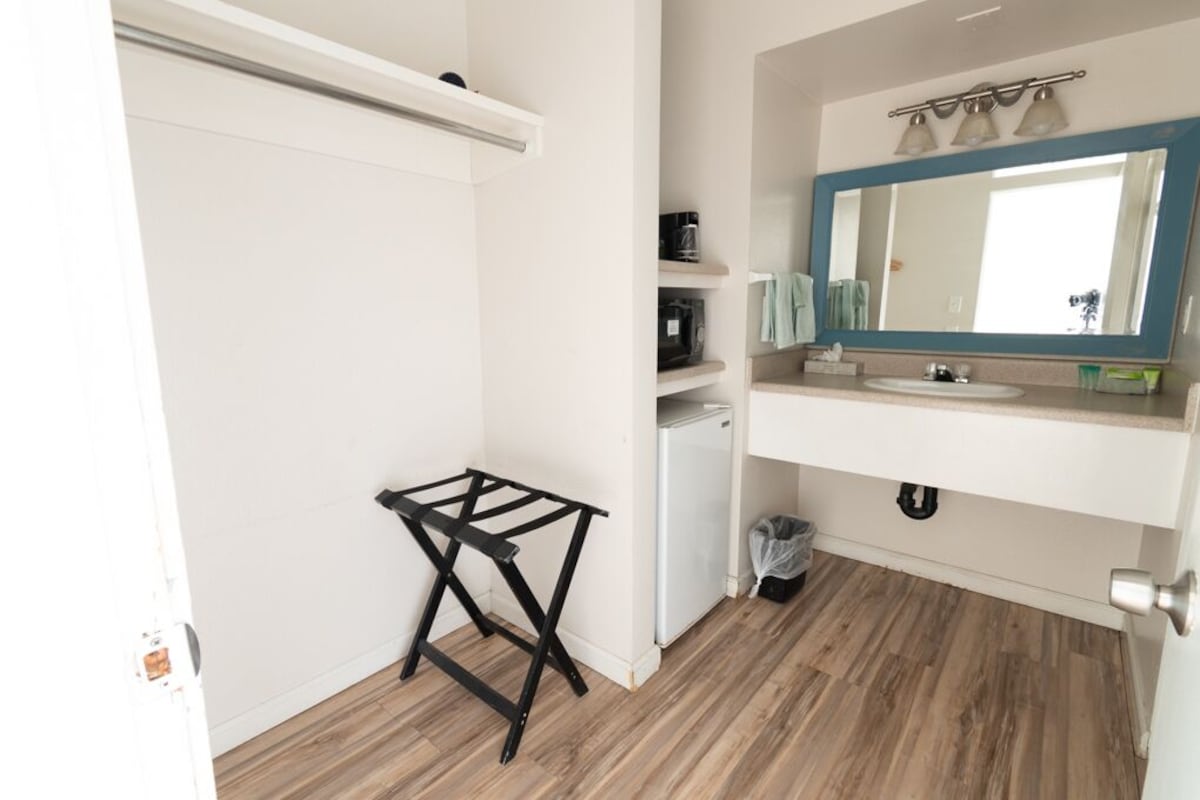 A bathroom with a white sink, a mirror with a blue frame, a small shelf with toiletries, and a black drying rack.