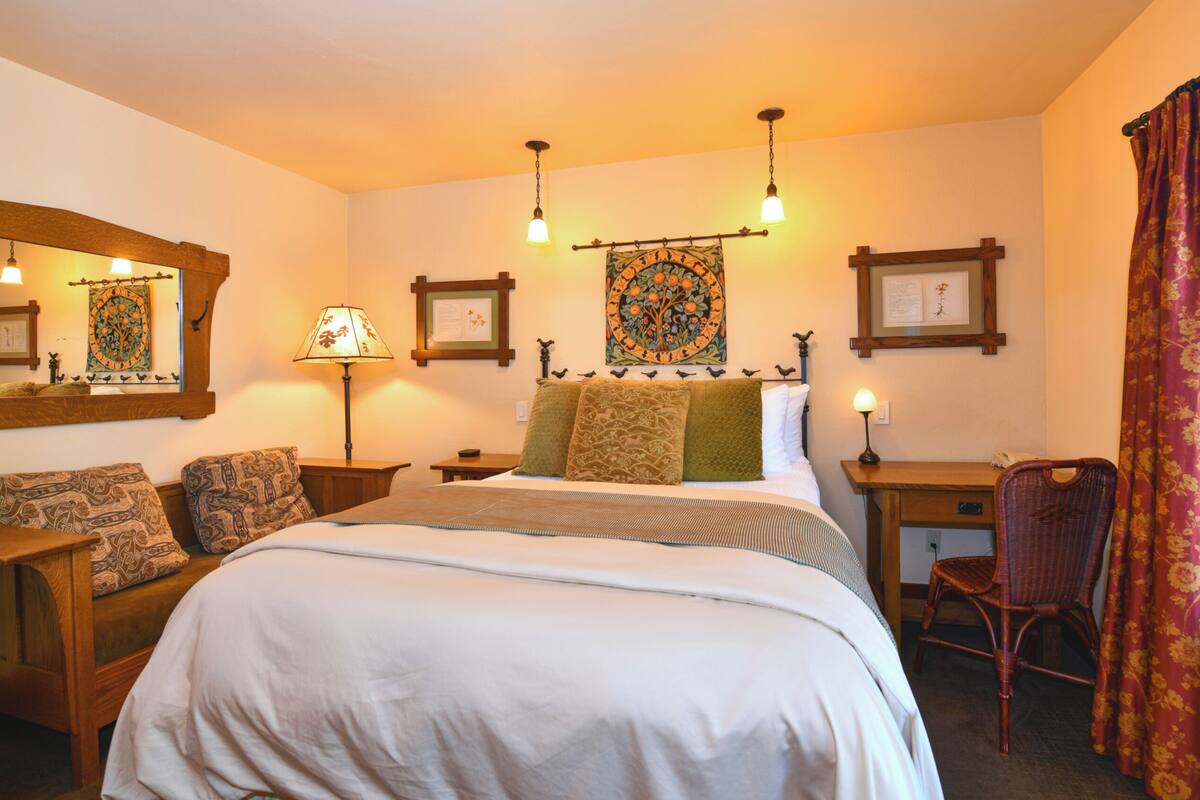 A hotel room with a large bed, a desk, a chair, and a window with curtains.