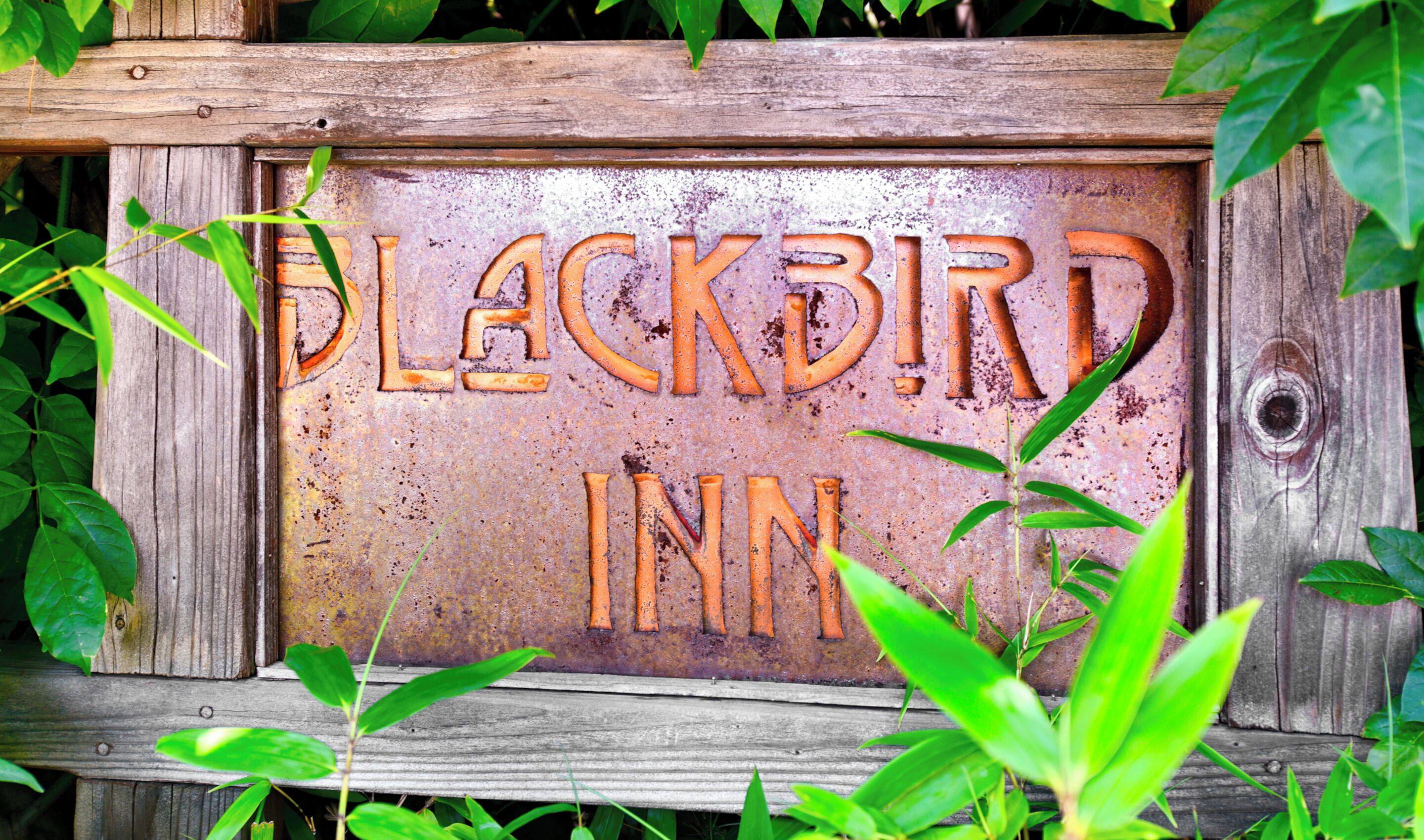 Un letrero de madera rústico con la frase 'BLACKBIRD INN' grabada.