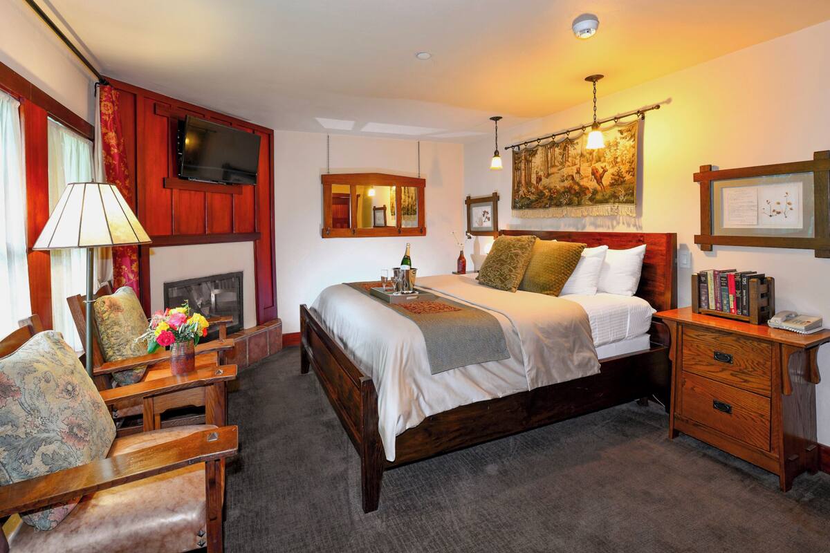 A hotel room with a bed, bedside table, lamp, chair, and a fireplace.