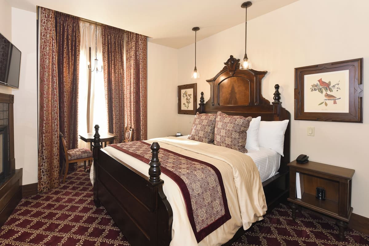 A traditional bedroom with a four-poster bed, a fireplace, a television, and a chandelier.