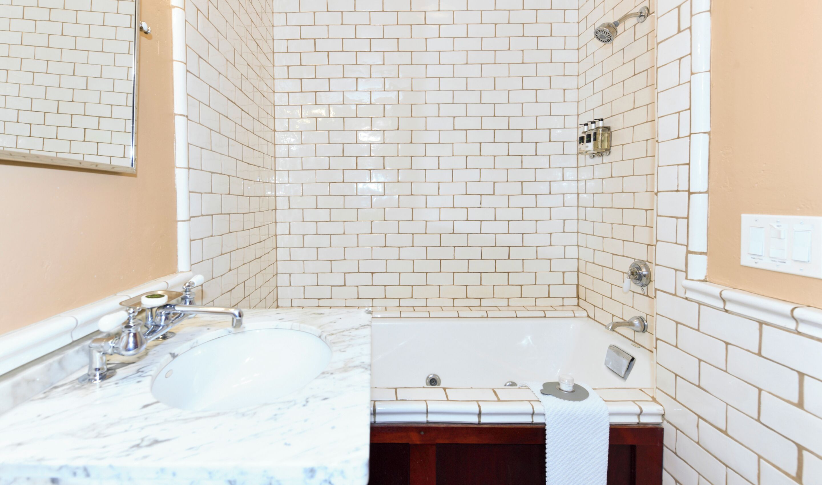 A bathroom with white subway tiles, a marble sink, a bathtub, and a mirror.