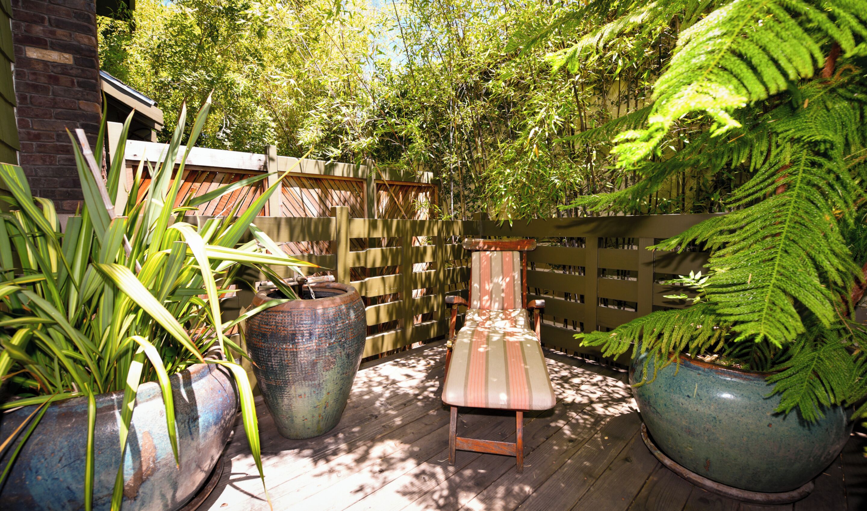 A wooden deck with a bench and large planters, surrounded by a wooden fence and lush greenery.