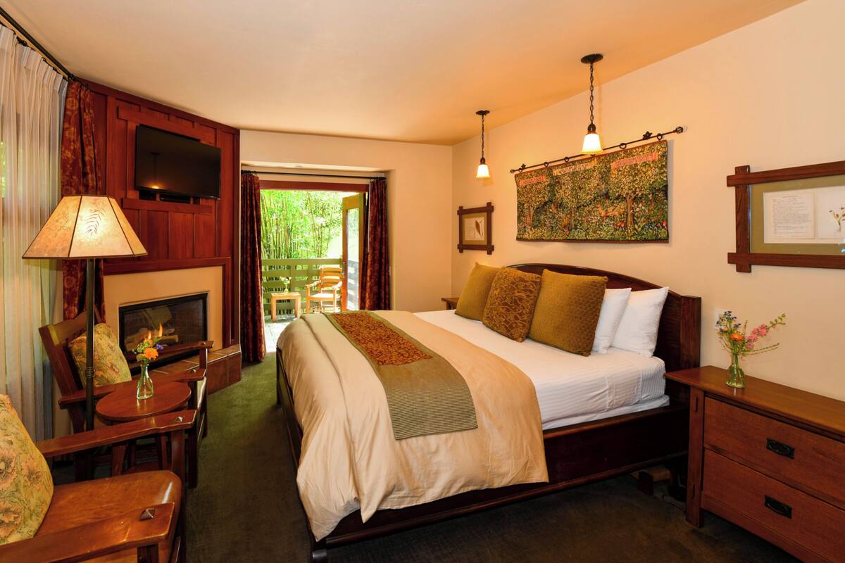 A bedroom with a bed, bedside table, lamp, chair, and a fireplace.
