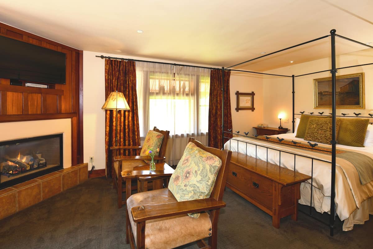 A bedroom with a four-poster bed, a fireplace, a desk, and a television mounted on the wall.