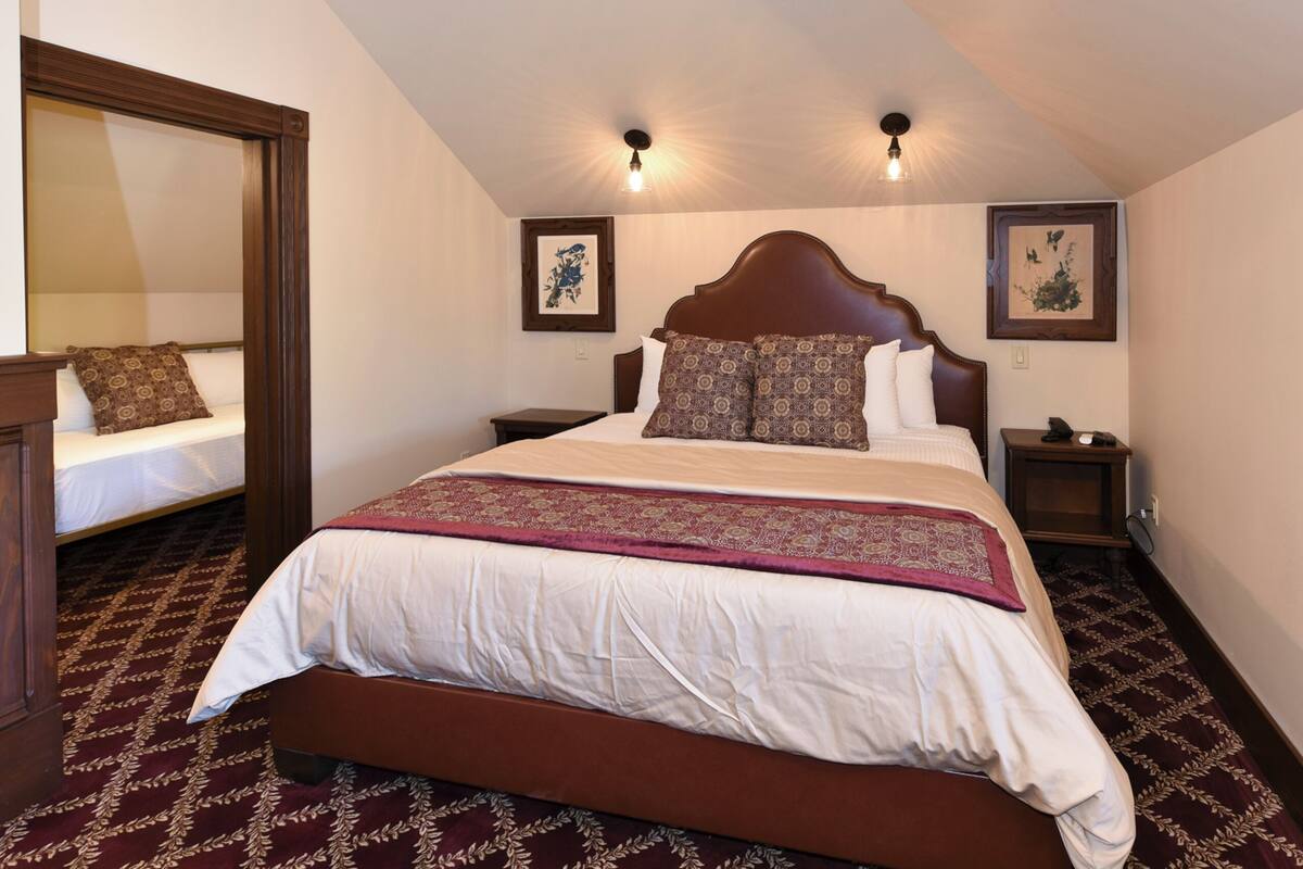 A neatly arranged bedroom with a large bed, two bedside tables, a nightstand, a mirror, and two wall-mounted lights.