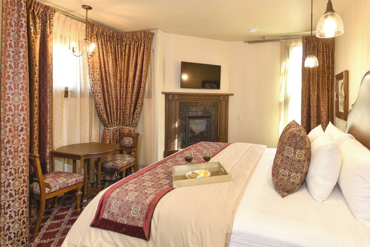 A hotel room with a bed, a table with chairs, a fireplace, and a television on the wall.