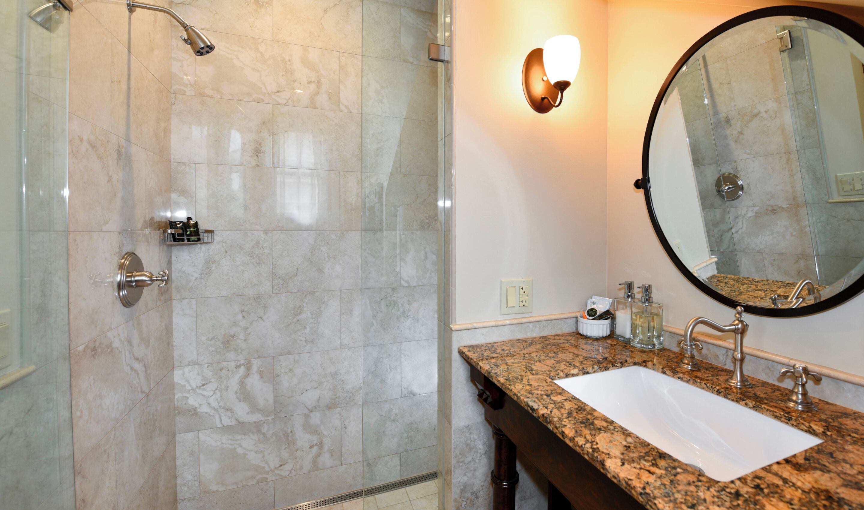 A bathroom with a shower, a sink, a mirror, and a wall-mounted light fixture.