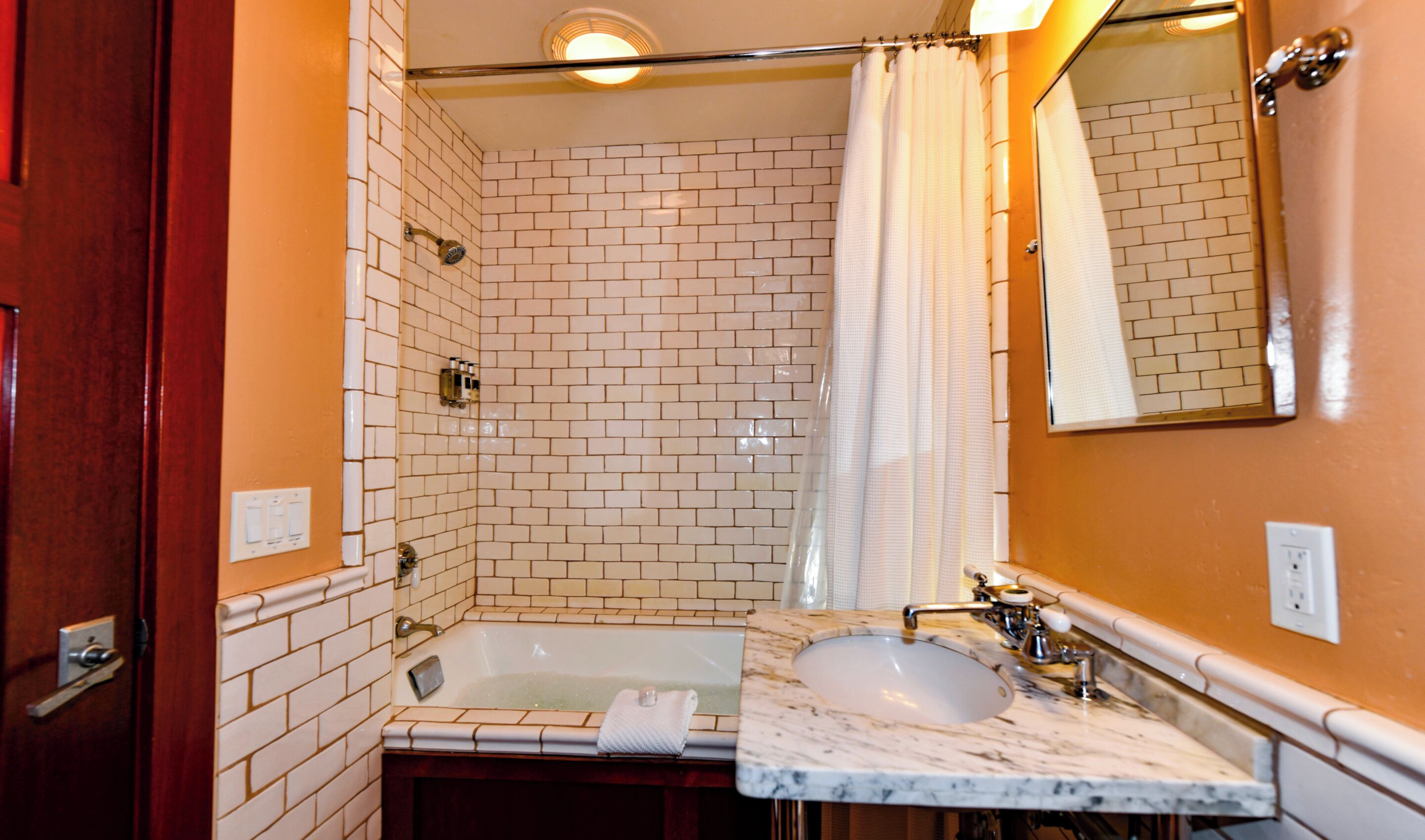 A bathroom with a white-tiled shower, a bathtub, and a marble sink.