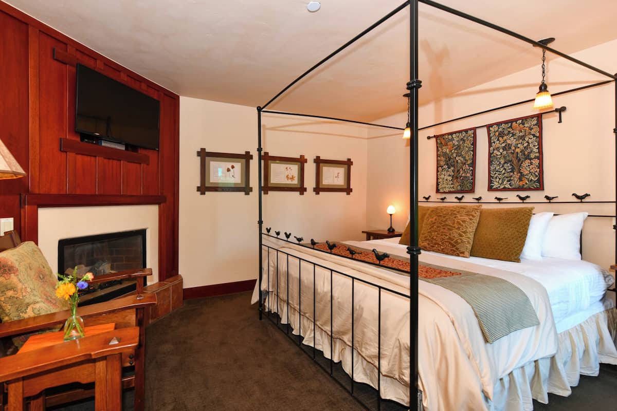 A four-poster bed with a canopy, a fireplace, a wooden chair, and framed certificates on the wall.