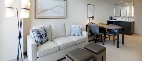 A modern living room with a sofa, a coffee table, a desk with a chair, and a large mirror.