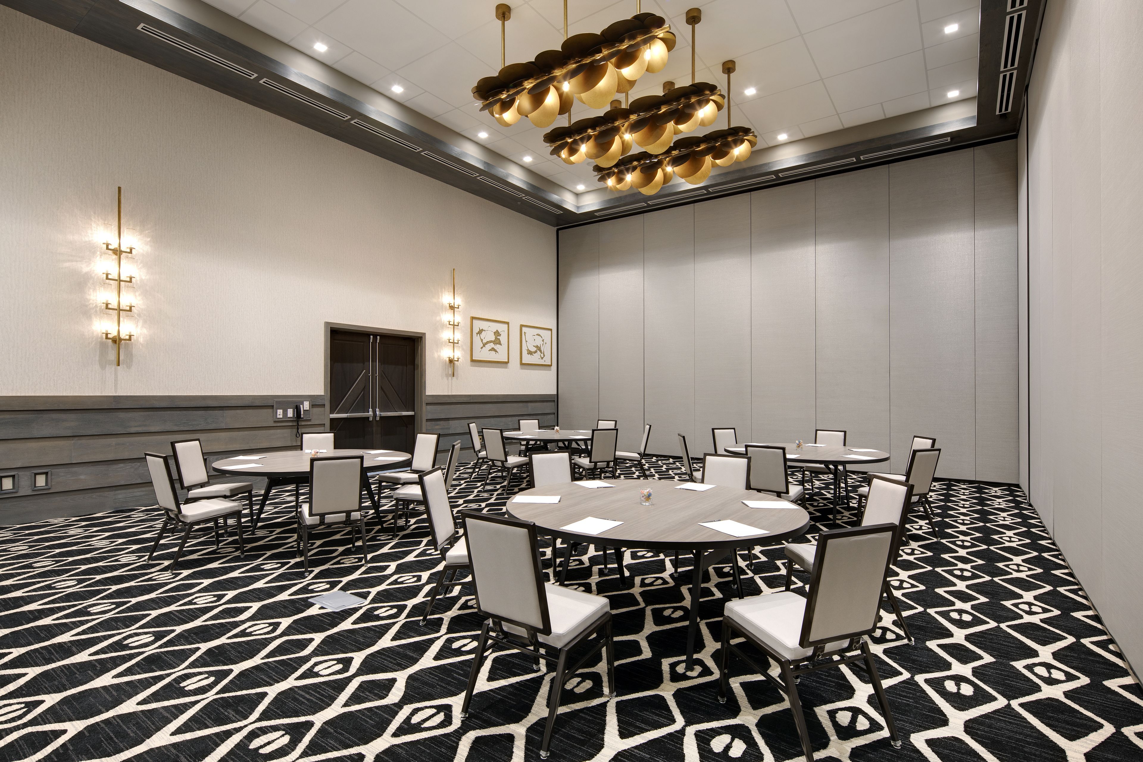 Un salón de conferencias con mesas y sillas redondas, una alfombra estampada y un candelabro en el techo.