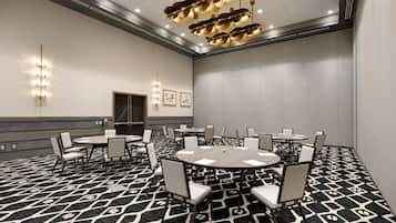 Un salón de conferencias con mesas y sillas redondas, una alfombra estampada y un candelabro en el techo.