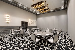 Une salle de conférence avec des tables et des chaises rondes, une moquette à motifs et un luminaire au plafond.