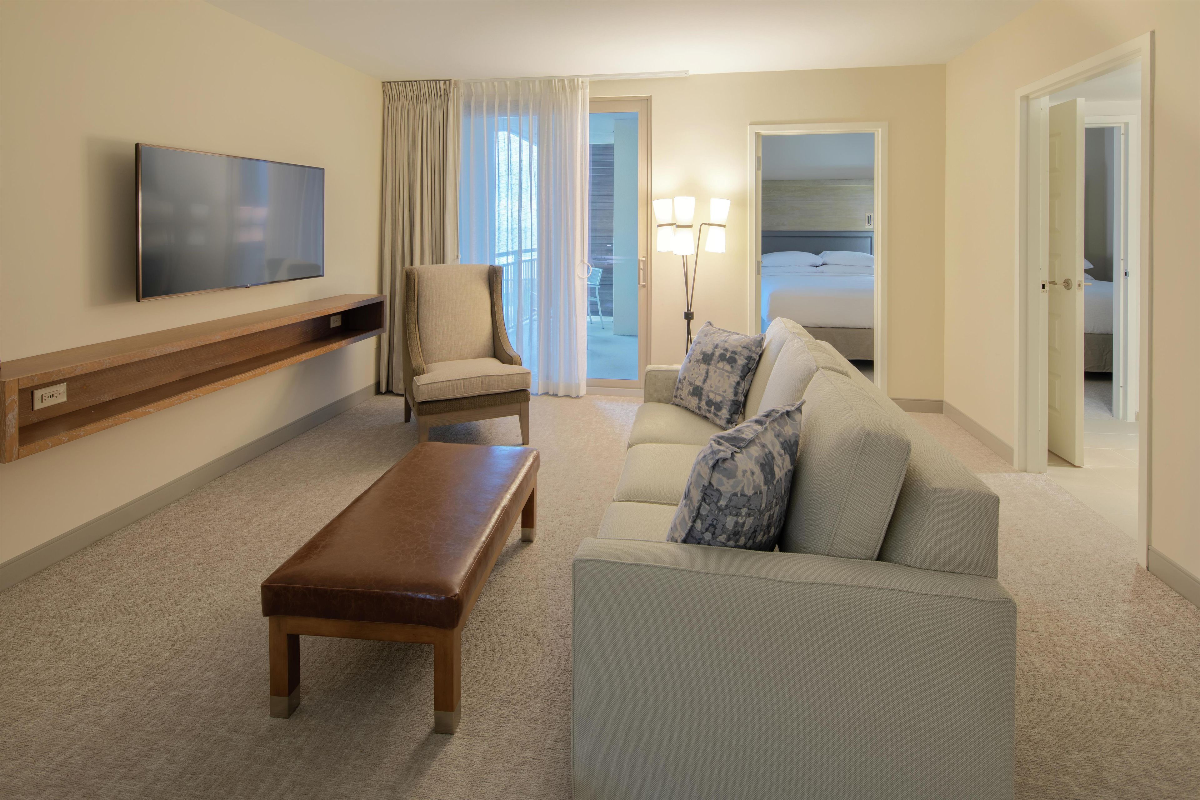 Quarto de hotel com televisão de tela plana, sofá, poltrona, banco e cama.